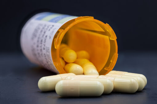 White pills with orange bottle. Pills spilling out of orange bottle. Blurry prescription tag is visible on the bottle. Foreground pills are in sharp focus, the rest of pills and bottle are blurry. Black natural background. Extremely sharp stock photo. Pill jar is open, cap is not visible on the image.